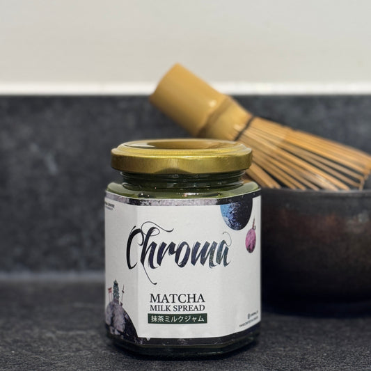 Jar of Chroma Matcha Milk Spread on a dark surface with a whisk in the background